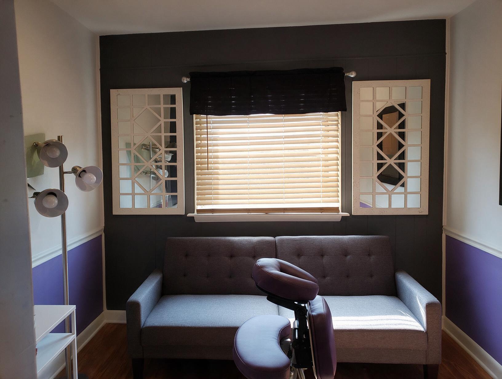 Empty treatment room with a gray sofa, purple massage chair, two white lattice mirrors