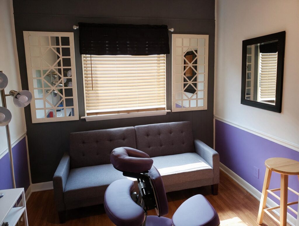 Tidy treatment room with a gray futon sofa under a window with blinds, mirrors